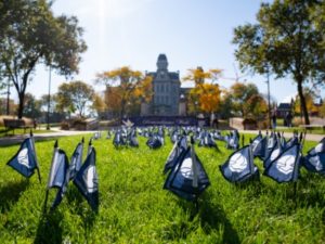 closeup of small flags signifying those who passed away in Pan Am 103 are placed in the grass overlooked by a large gothic building.
