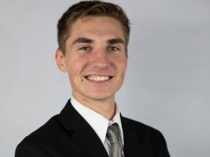 headshot of a man smiling at the camera in front of a gray background