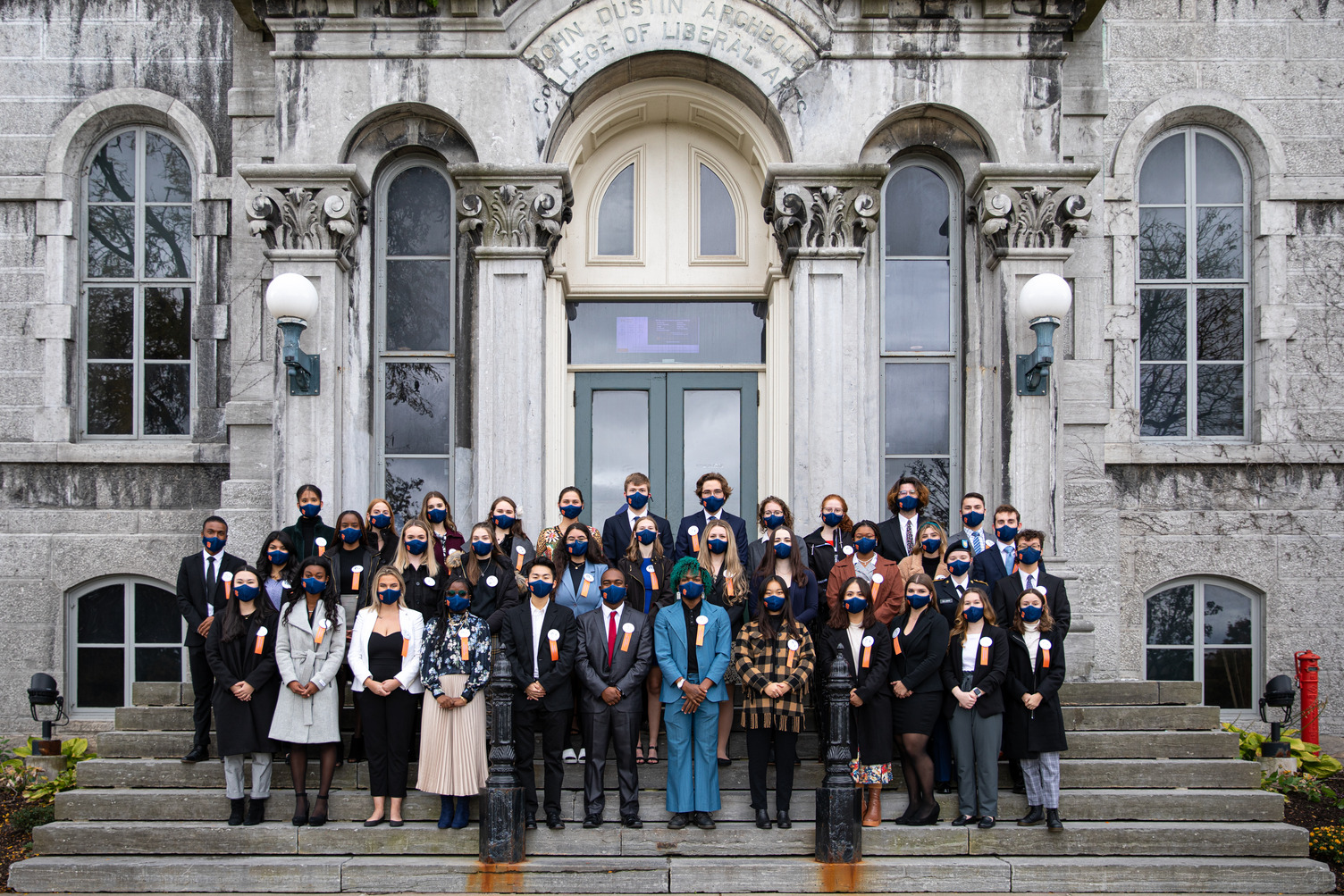 group photo of 37 students standing in front of an old gray stone building.