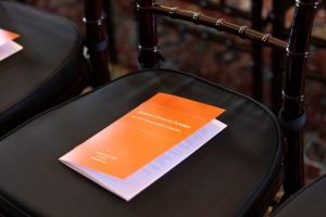 An orange program titled "Syracuse University Scholars Reception" rests on a black cushioned chair