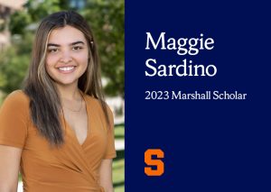 This is a rectangular image and on the left is a headshot of a woman smiling at the cameral with long brown hair and a V-neck camel-colored blouse, and on the right is the text "Maggie Sardino, 2023 Marshall Scholar" on the right in white, in front of a dark blue background. The Syracuse block S is in the bottom left corner.