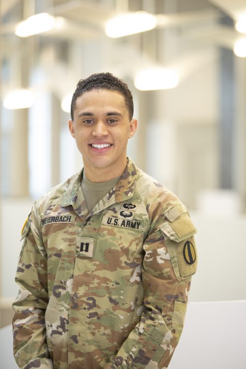 Man in U.S. Army uniform stands smiling, the camera focused on him from the waist up.